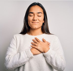 Photo of Girl in white sweater with both hands over her heart